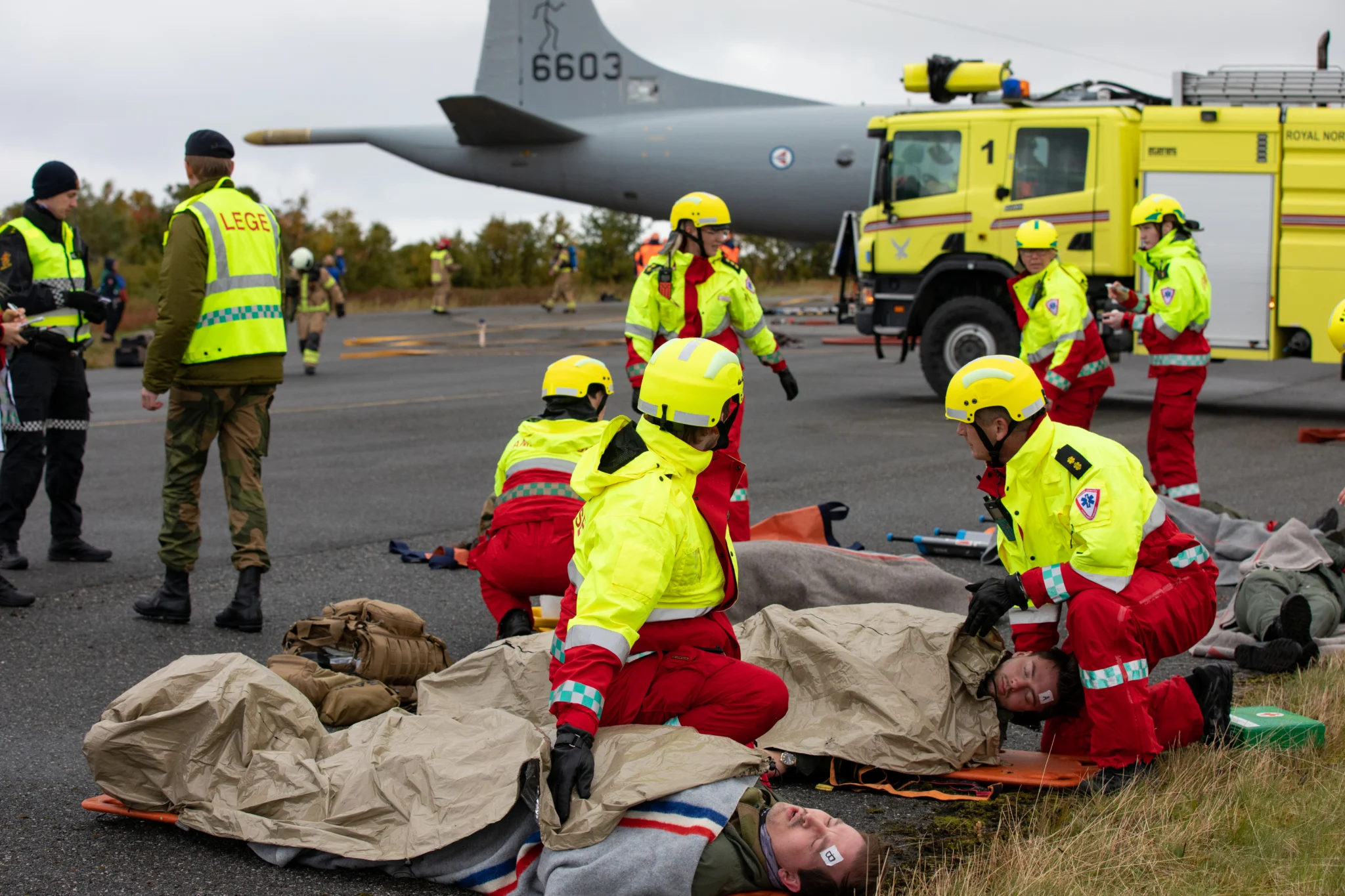 Ambulansepersonell arbeider med øvingspasienter på bårer under en tverretatlig øvelse. LESS-bårer er synlige på samleplassen.