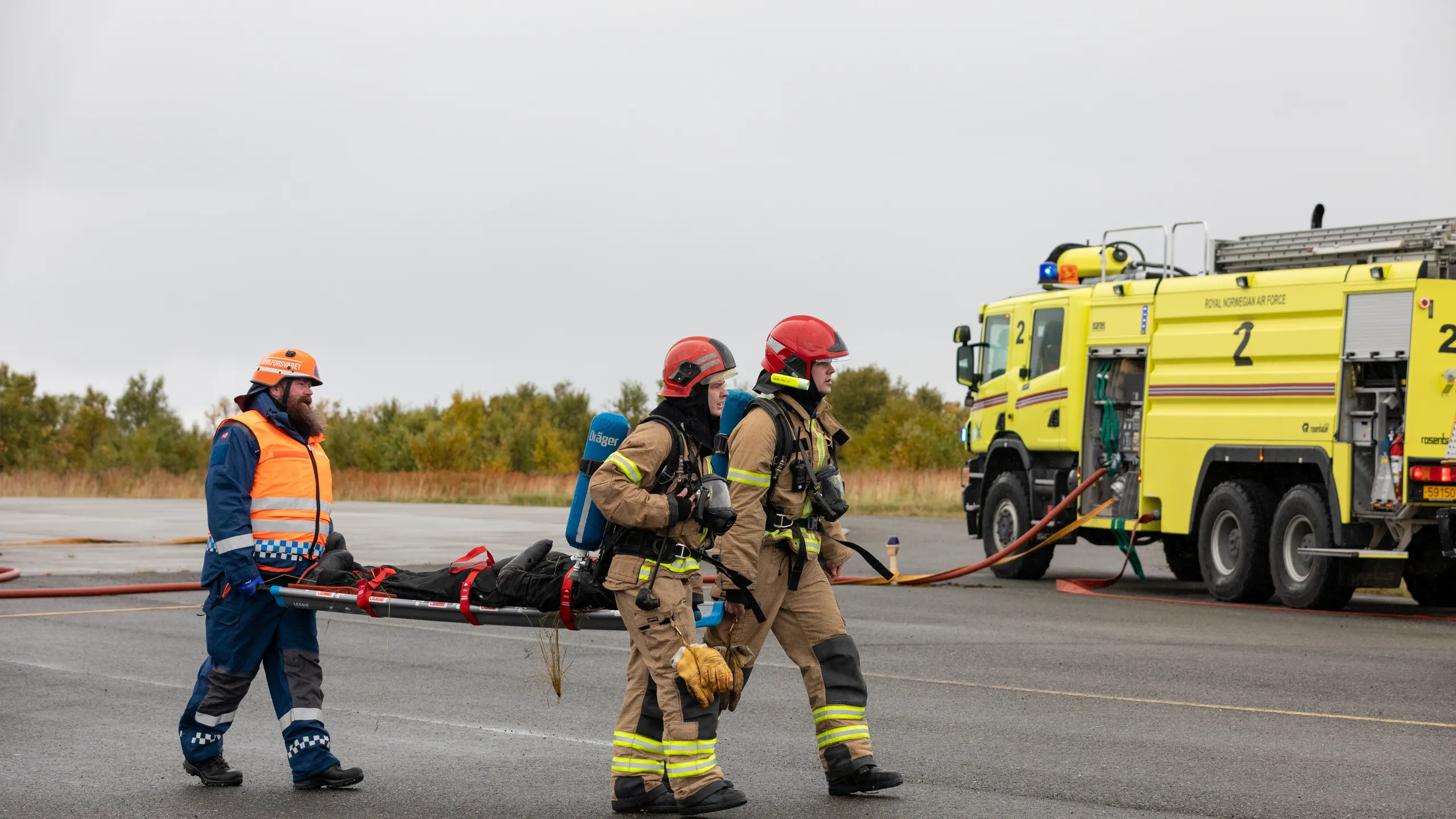 Sivilforsvaret og brannmannskap bærer en øvingspasient på en LESS-båre med blå håndtak.